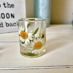 a glass with daisies painted on it sitting on a table next to other items