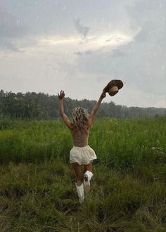 a woman is running through the grass with her arms in the air