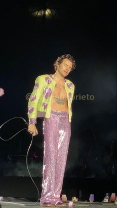 a man in pink pants and yellow jacket on stage with his hair dryer attached to his chest