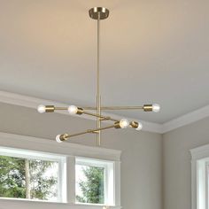 a modern chandelier hanging from the ceiling in a living room with white walls and windows