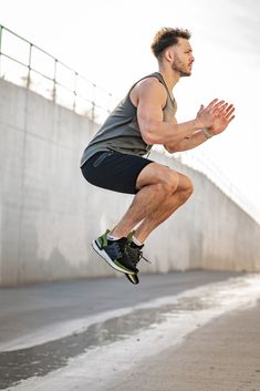 a man is jumping in the air with his feet up while wearing black shorts and a gray tank top