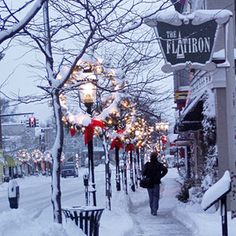 a person walking down a snow covered sidewalk in front of shops and restaurants at christmas time