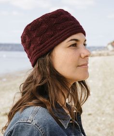 a woman wearing a red knitted hat on the beach looking off into the distance