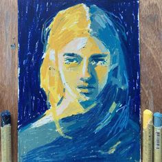 a painting of a blonde haired woman in blue and yellow on a wooden table next to some crayons