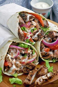 three pita sandwiches with meat and vegetables on a cutting board