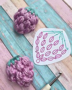 two balls of yarn sitting next to a crochet hook on a wooden surface