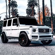 a white mercedes g - class is parked in front of palm trees