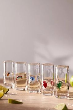 four shot glasses filled with different types of drinks and limes on a wooden table