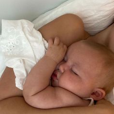 a woman holding a baby in her arms on top of a white sheet covered bed