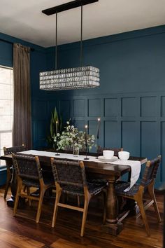 a dining room with blue walls and wooden flooring, chandelier above the table