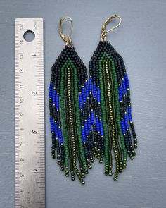 a pair of blue and green seed beaded earrings next to a measuring ruler on a gray surface