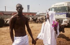 a man and woman holding hands walking in front of a truck with cows behind them