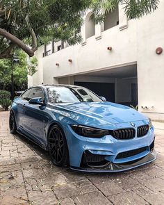 a blue bmw car parked in front of a building next to a parking lot with trees