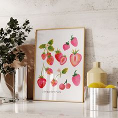 a framed strawberry print sitting on top of a white shelf next to a potted plant