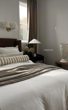 a bed with white sheets and pillows in a bedroom next to a lamp on a night stand