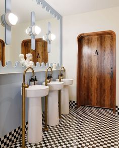 a bathroom with two sinks and three mirrors on the wall next to a wooden door