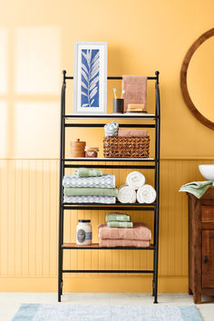 a bathroom with yellow walls and black shelving unit filled with folded towels, toiletries and other items