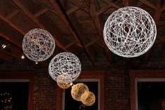 some white balls hanging from the ceiling with lights on them in front of a brick building