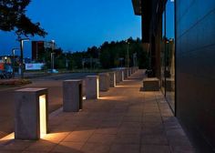 a row of concrete benches sitting next to each other on a sidewalk at night time