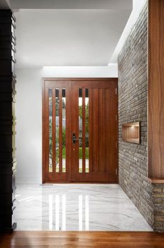 an entryway with two wooden doors and white marble flooring in front of a brick wall