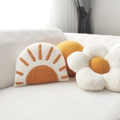 two decorative pillows sitting on top of a white couch next to a flower shaped pillow