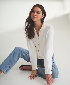 a woman is sitting on the floor wearing jeans and a white cardigan sweater with buttons