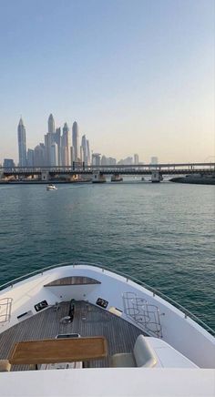 the back end of a boat traveling on water with city skyline in the background at dusk