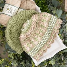 two crocheted blankets on a white plate next to green leaves and a ball of yarn