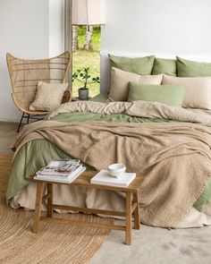 a bed with green sheets and pillows in a room next to a chair, table and window