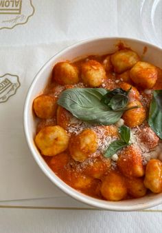 a white bowl filled with food on top of a table next to a fork and napkin