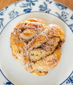 two cinnamon buns on a blue and white plate covered in powdered sugar sitting on top of a wooden table