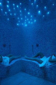 two women laying on their backs in a blue tiled room with lights hanging from the ceiling