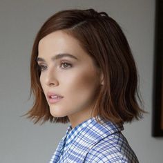 a woman with short brown hair wearing a blue and white checkered shirt is looking at the camera