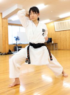 a man standing on one leg while wearing a black belt and white karate outfit, in a room with wood floors