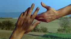 two hands reaching out towards each other in front of a blue sky and green field