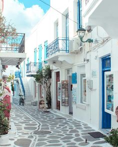 an alley way with white buildings and blue doors on both sides, surrounded by greenery