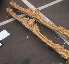 an ornately carved wooden frame laying on the ground next to a parking lot with other items