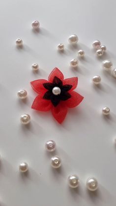 a red flower with black center surrounded by white pearls and other beads on a table