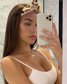 a woman taking a selfie in front of a mirror wearing a white top and headband