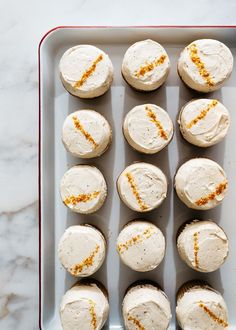 twelve cupcakes with white frosting and orange sprinkles on a tray