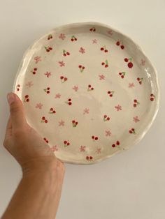 a hand is holding a white plate with red flowers on it and cherries all over the rim