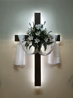 a cross with flowers on it in front of the light coming from behind curtaines
