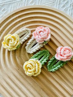 four crocheted flowers sitting on top of a wooden plate