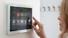 a woman is touching the buttons on a wall mounted touch screen device in her home
