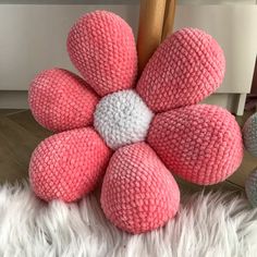 a pink and white knitted flower sitting on top of a fluffy white rug next to a wooden pole