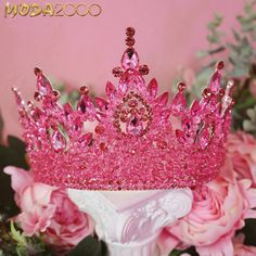 a pink tiara sitting on top of a white vase filled with flowers and greenery