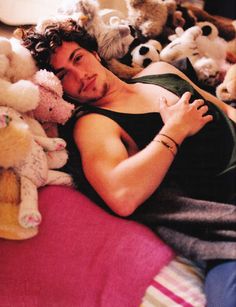 a man laying in bed surrounded by stuffed animals