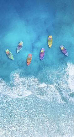 five colorful surfboards floating in the ocean next to an aerial view of the beach