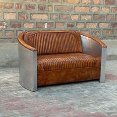 a brown leather couch sitting on top of a brick floor next to a stone wall