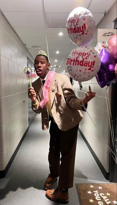 a man in a suit and tie holding balloons with the words happy birthday on them
